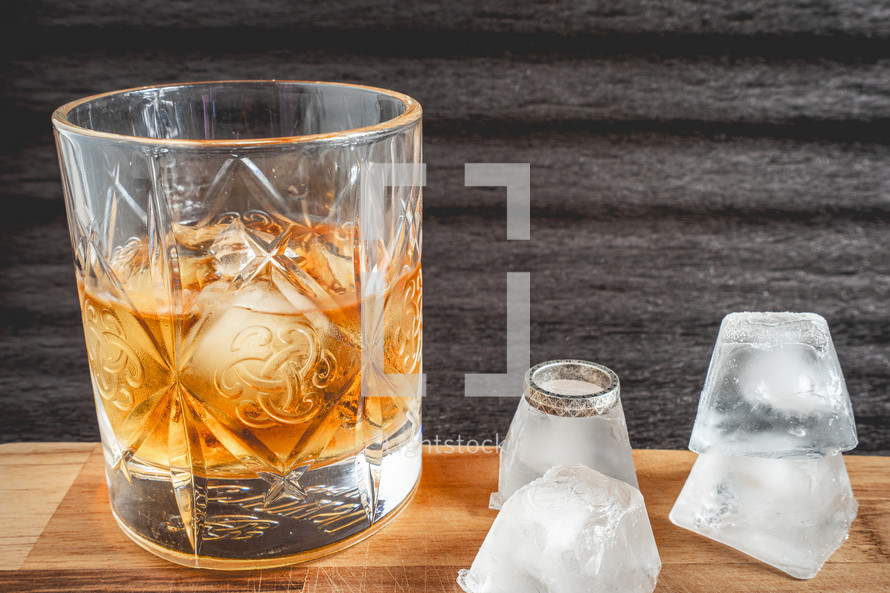 A glass of wiskey on the Rocks, on a black background, and a wooden table with wedding ring.