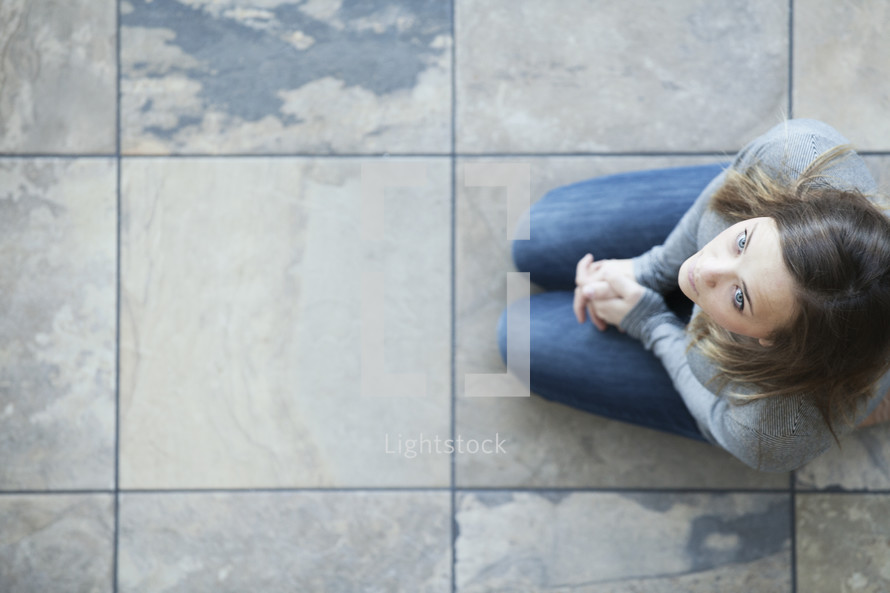 Aerial view of woman praying on her knees on tiles.