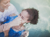 Man baptizing a girl in a pool of water.