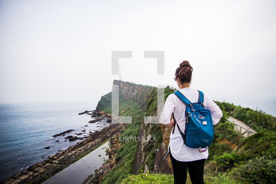 woman standing at the edge of a cliff looking out at the ocean 