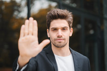Portrait of young businessman disapproval gesture with hand: denial sign, no sign, negative gesture closes the camera with hand, professional male manager wearing suit jacket