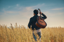 A young man standing in a field with a guitar over the back