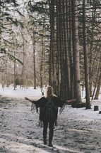 a woman standing with outstretched arms in a snowy forest 