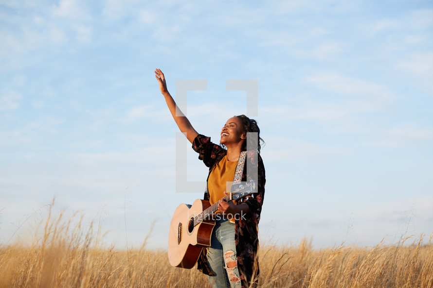 a woman standing in a field playing a guitar 