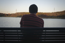 man sitting on a bench looking at water 