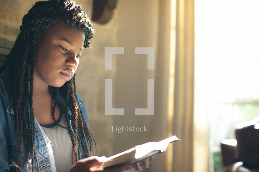 Woman reading the Bible by a window.