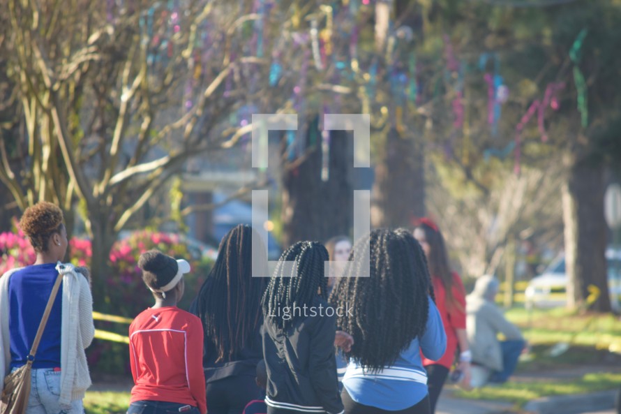 African American girls walking down a street under a tree covered in Mardi Gras beads 