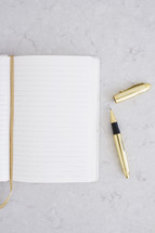 An open blank notebook and a gold pen.