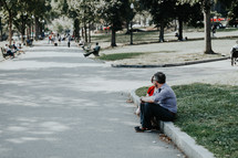 people sitting along the walkway of a busy park 