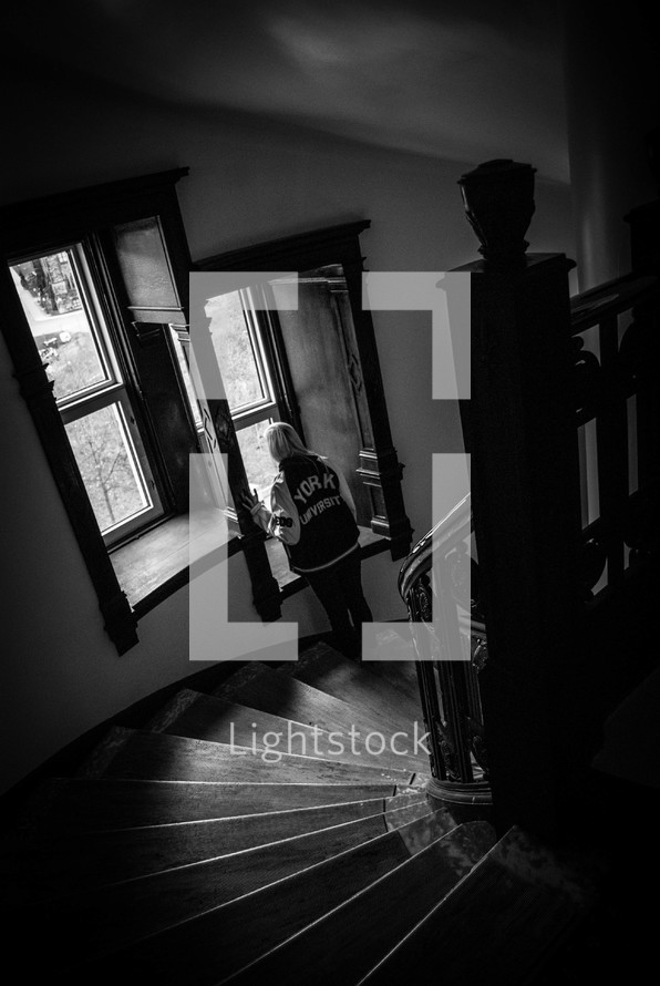 woman standing in a stairway looking out a window