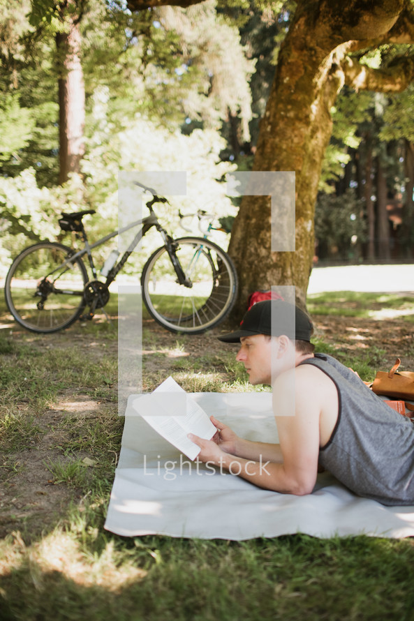 man reading a book lying on a blanket in the grass 