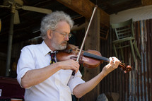 a man standing in a barn playing a fiddle 