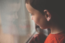 A boy stands looking out of a window.