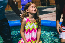 A little girl in a small swimming pool, preparing to be baptized.