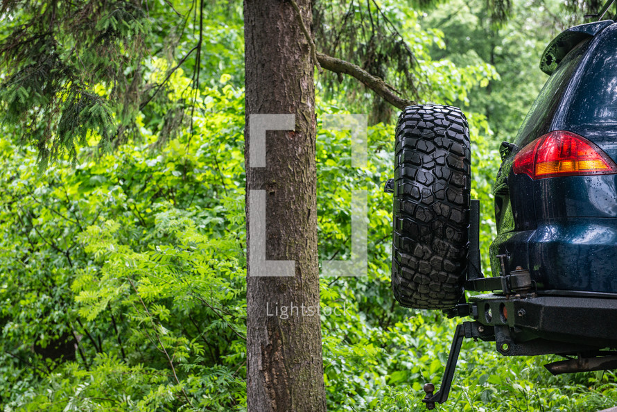 the back of a jeep with a wheel parked in the forest