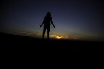 Silhouette of a woman standing before a sunset.