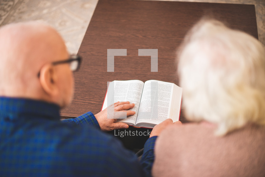 an elderly man and woman reading a Bible together 