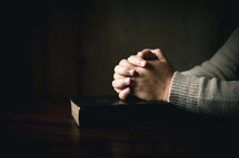 Man praying with folded hands in a dark room