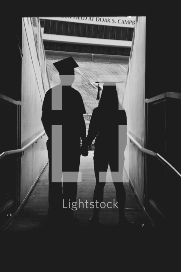 silhouette of graduate couple holding hands 