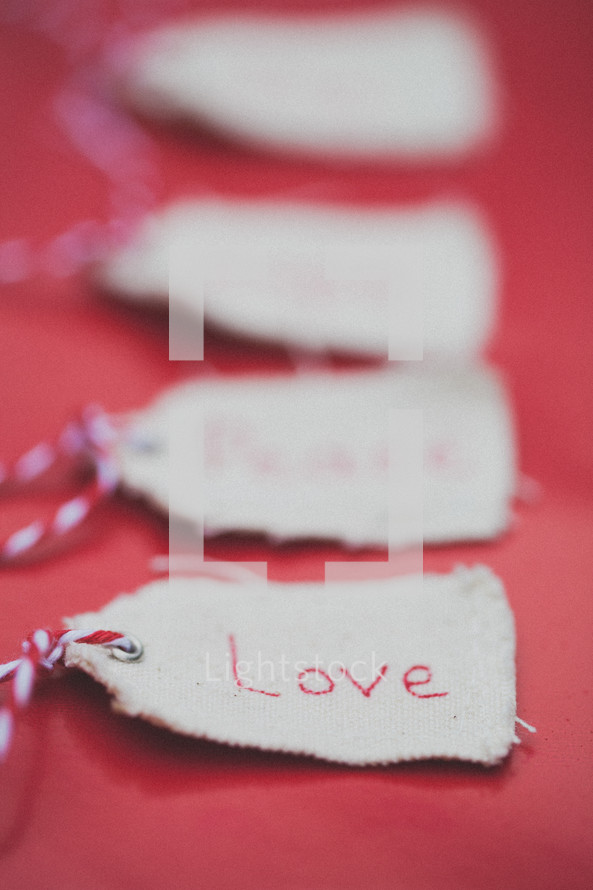 Christmas gift tags lined up in a row, the first one reading "Love," on a red background.