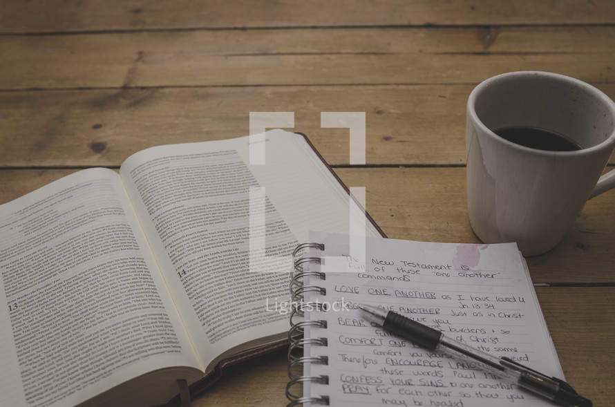 open Bible, coffee mug, pen, and notes on a notepad 