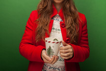 a woman in a red peacoat holding a mug 