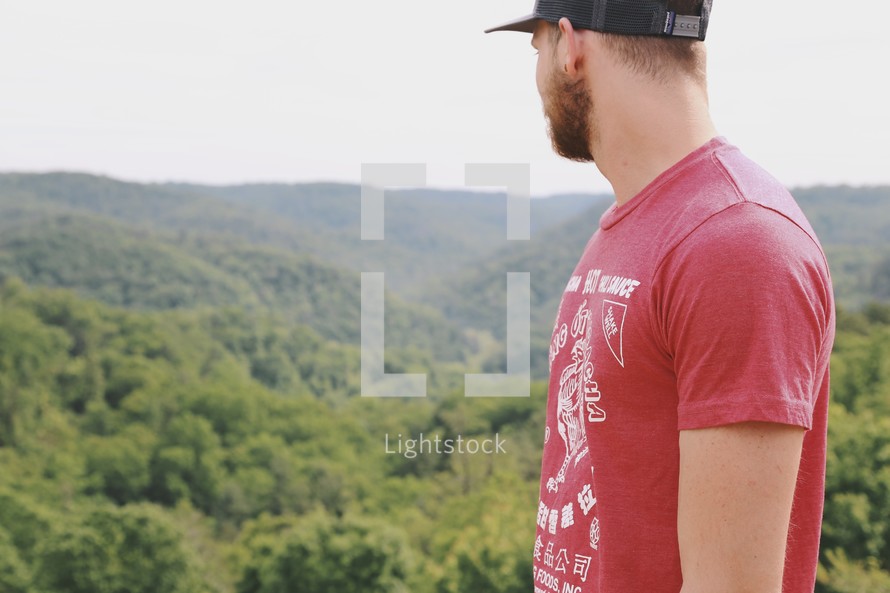 man in a ball cap looking out at mountains 