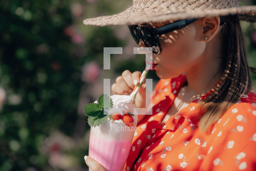 Pretty woman drinking strawberry milkshake cocktail with straw, nature backdrop. High quality photo