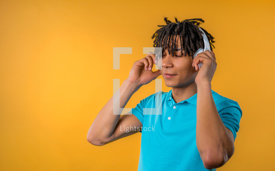 Positive young african american man listening music, enjoying dance with headphones on yellow studio background. Radio, wireless modern sound technology, online player. High quality. 