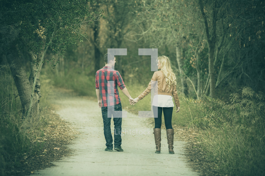 A couple walking holding hands on a nature trial. 