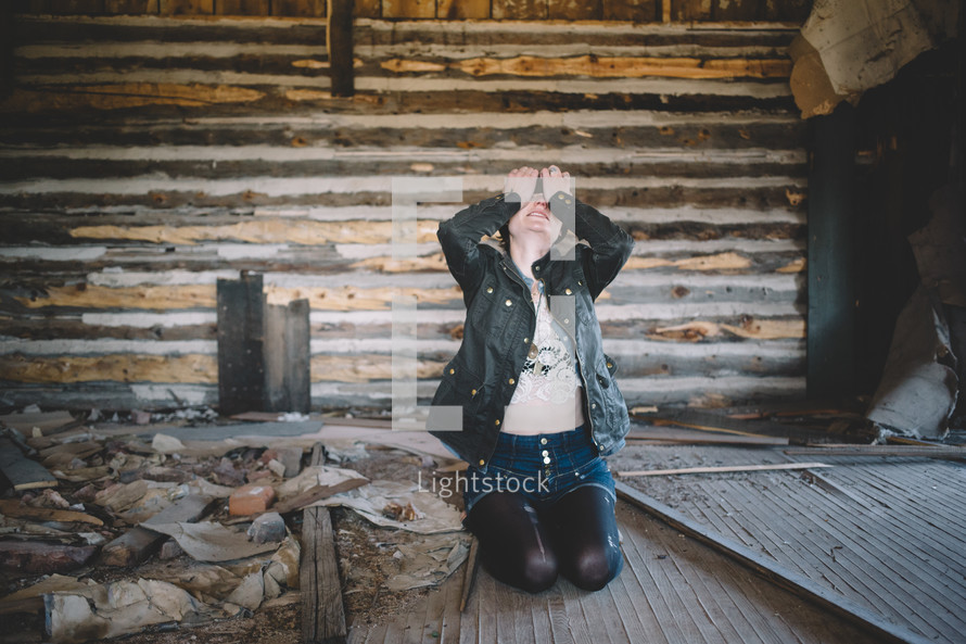A woman sits with head in hands in an abandoned log house.