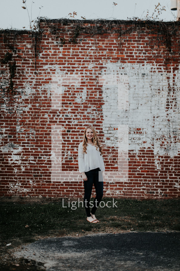 portrait of a young woman standing in front of a brick wall 