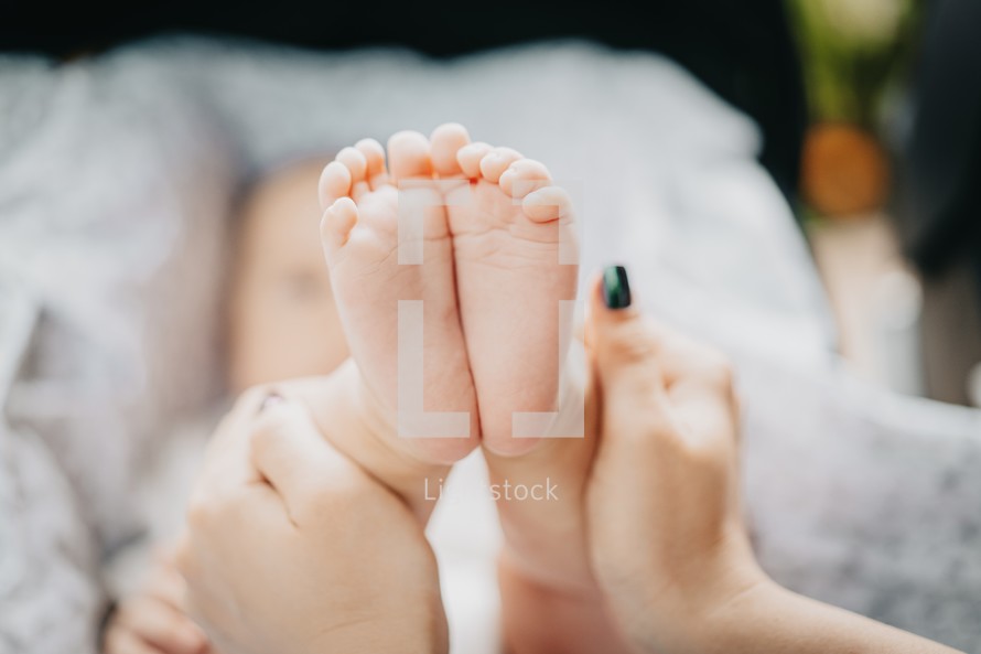 Mother holding little baby boy feet in hands.