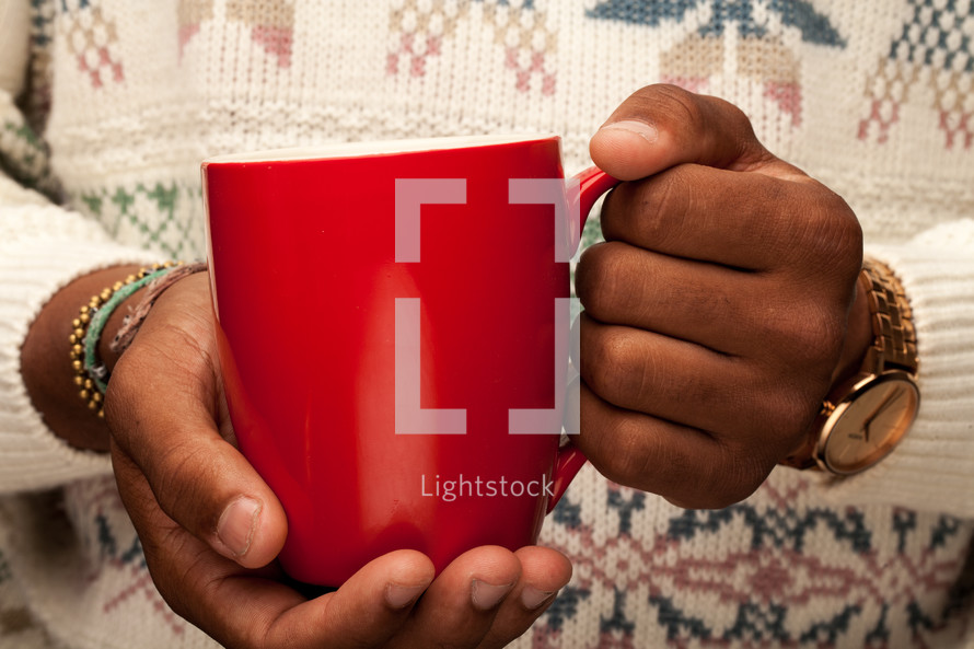 a man in a sweater holding a red coffee mug 