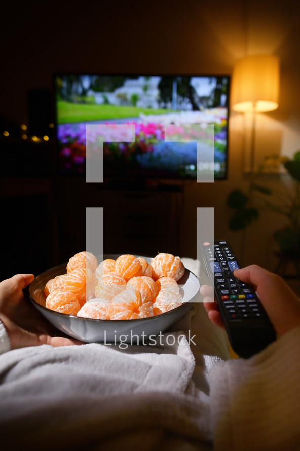 Closeup Woman Eating Tangerine And Watching TV On Bed