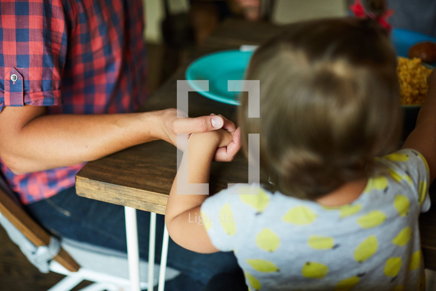 family holding hands in prayer around a dinner table 