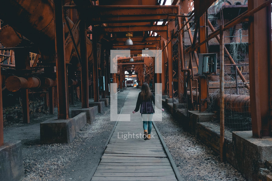 a woman walking under rusty steel beams 