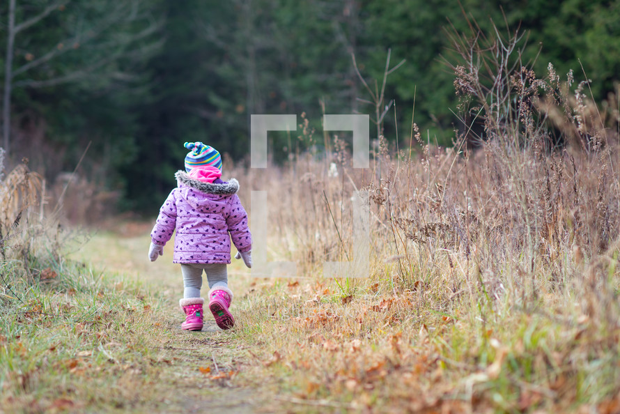 a toddler walking through a field 