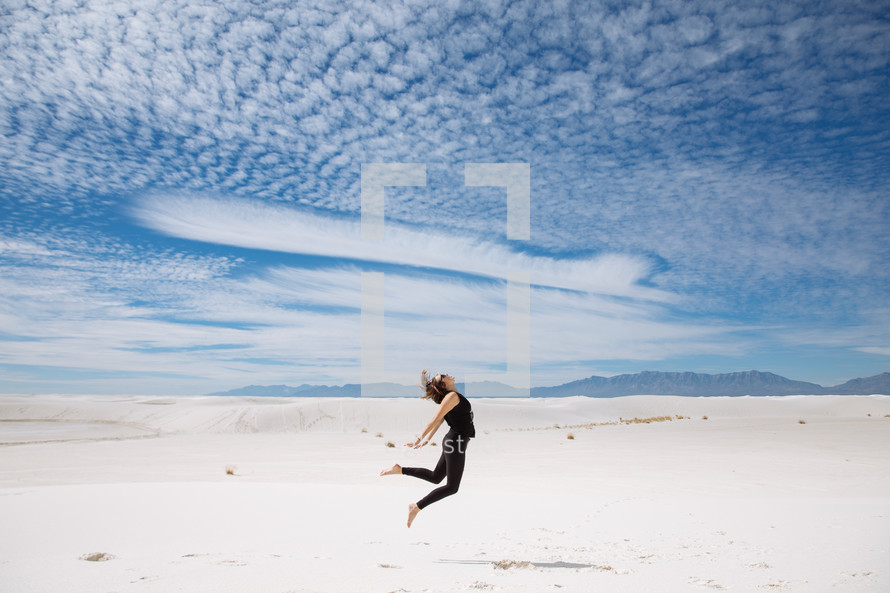 a woman leaping up over sand in a desert 