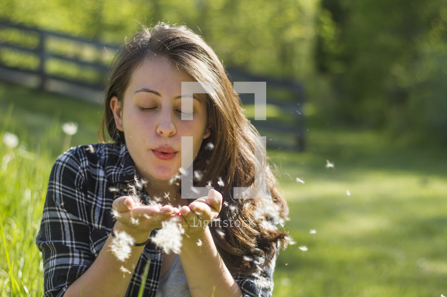Woman sitting in a field blowing dandelion seed heads.