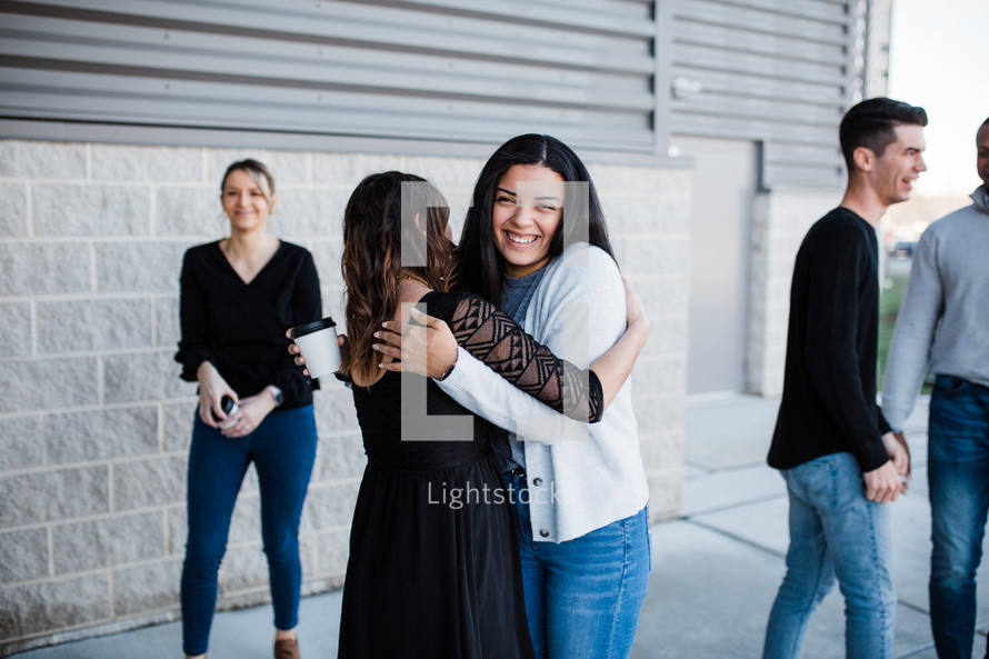 two women hug in front of a church 