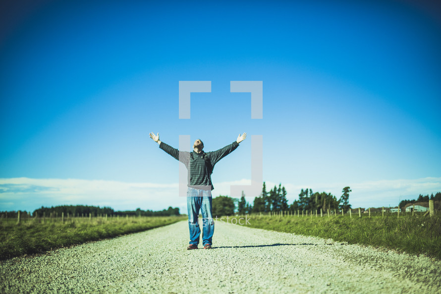 man standing in the middle of a road with hands raised to God 