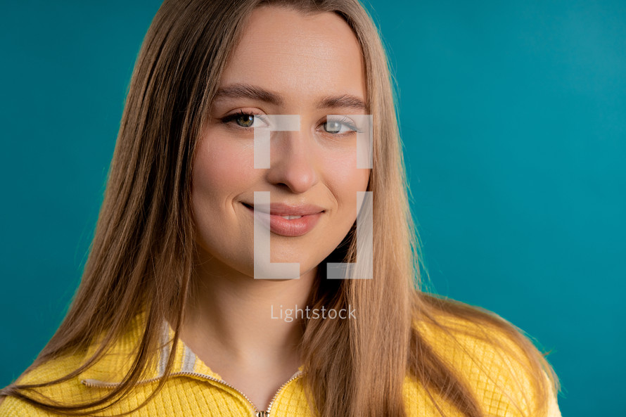 Young portrait woman in yellow sweater looking to camera on blue studio background. Pretty blonde female smiling model.