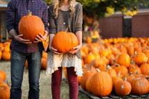 a couple standing holding pumpkins in a pumpkin patch 