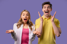 Amazed happy couple expresses WOW. Impressed man woman. Great, unbelievable news, trying to get attention. Concept of sales, profitable offer. Excited friends on violet background. High quality 