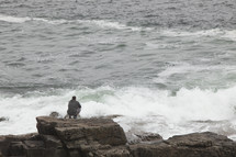 man watching waves crashing into rocks 