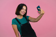 Smiling happy woman making selfie on smartphone over pink background. Technology, mobile device, social networks concept.
