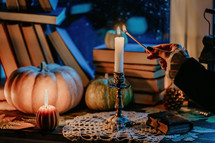 Rich retro dressed woman hand lights candle in bronze candlestick with long match. Timeless, vintage, autumn. Cozy ambience of fall. Promotions or tranquil visual storytelling. High quality photo