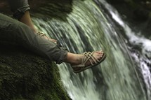 feet hanging over an edge near a waterfall 
