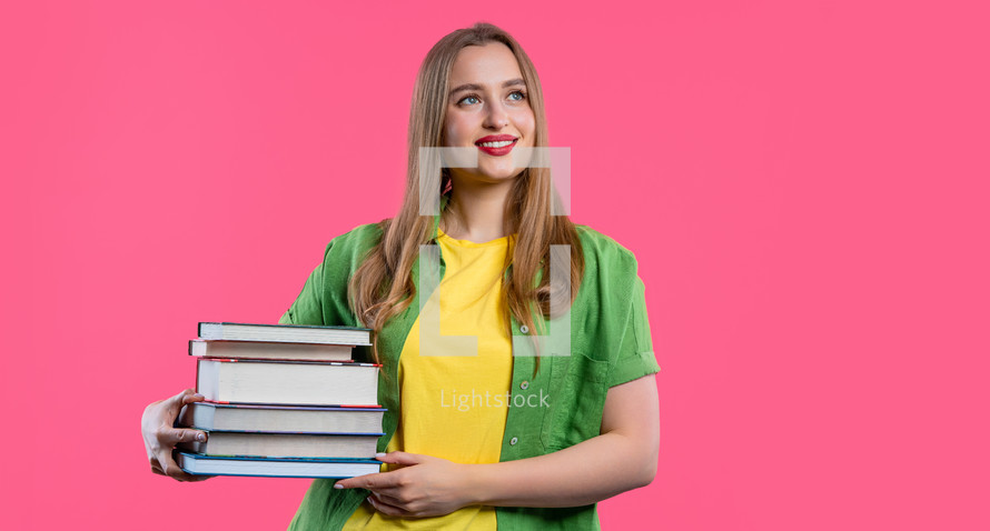Smiling student woman with stack books from library, pink background. Copy space. Happy girl smiles, she is happy to graduate. High quality